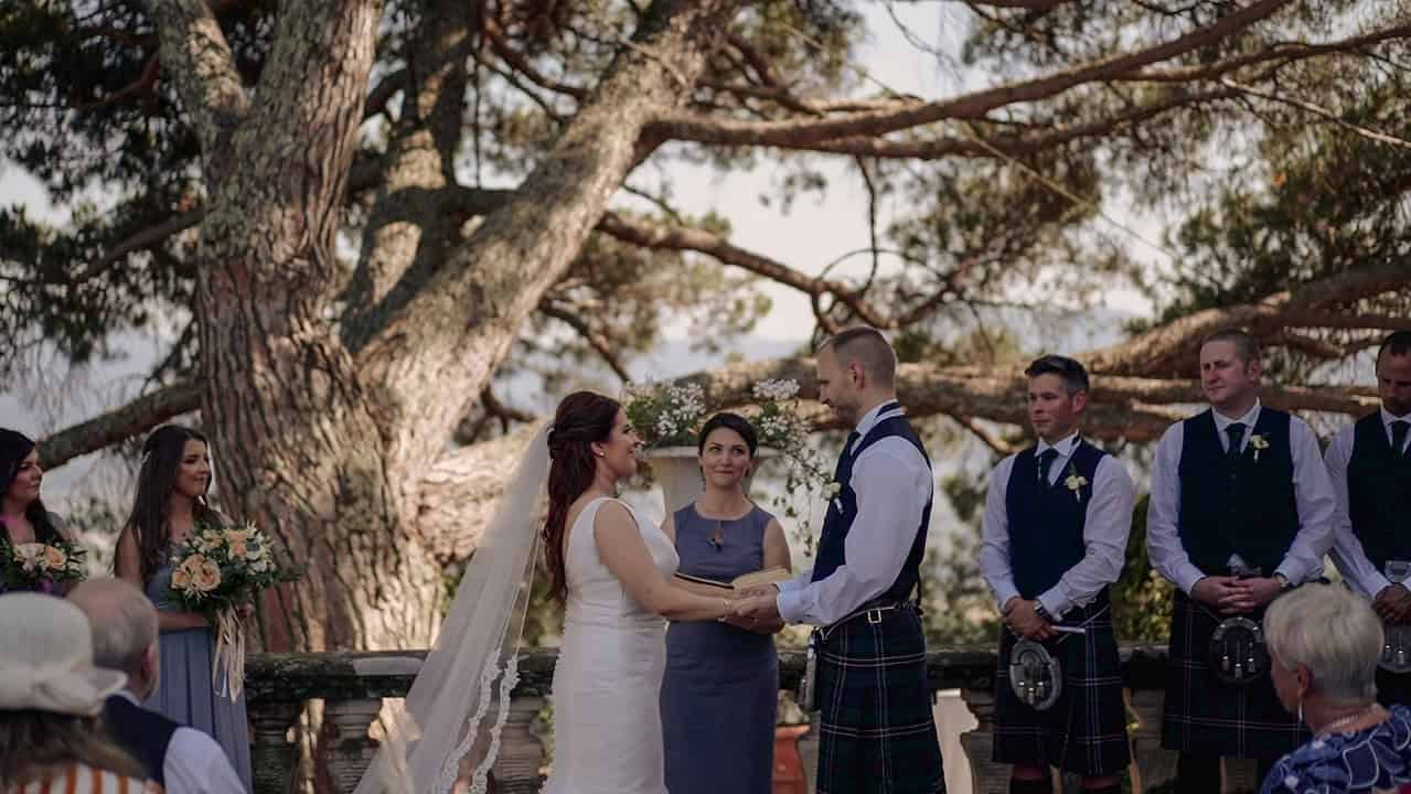 Kathryn and Ross hold each other hands, Carina - the wedding officiant - is reading their love stories.